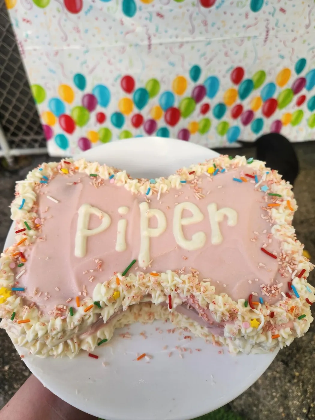 A bone-shaped cake with pink icing and rainbow sprinkles
